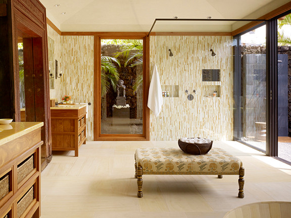 Modelo de cuarto de baño principal tropical extra grande con puertas de armario de madera oscura, ducha abierta, paredes beige, suelo de travertino, lavabo bajoencimera y encimera de piedra caliza