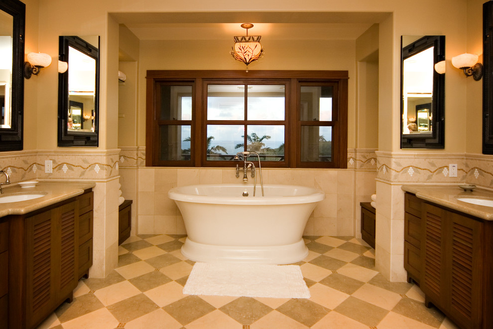 ハワイにあるトロピカルスタイルのおしゃれな浴室 (アンダーカウンター洗面器、ルーバー扉のキャビネット、濃色木目調キャビネット、置き型浴槽、ベージュのタイル) の写真