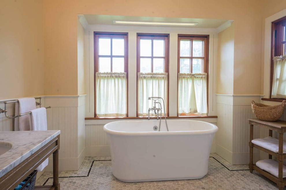 Modelo de cuarto de baño principal campestre de tamaño medio con armarios abiertos, bañera exenta, paredes beige, suelo de baldosas de cerámica, lavabo bajoencimera, encimera de mármol y suelo gris