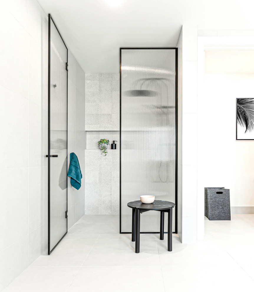 This is an example of a large modern ensuite bathroom in Melbourne with flat-panel cabinets, black cabinets, a freestanding bath, a built-in shower, a one-piece toilet, white tiles, porcelain tiles, white walls, porcelain flooring, a submerged sink, engineered stone worktops, white floors, a hinged door, white worktops, a wall niche, double sinks and a floating vanity unit.