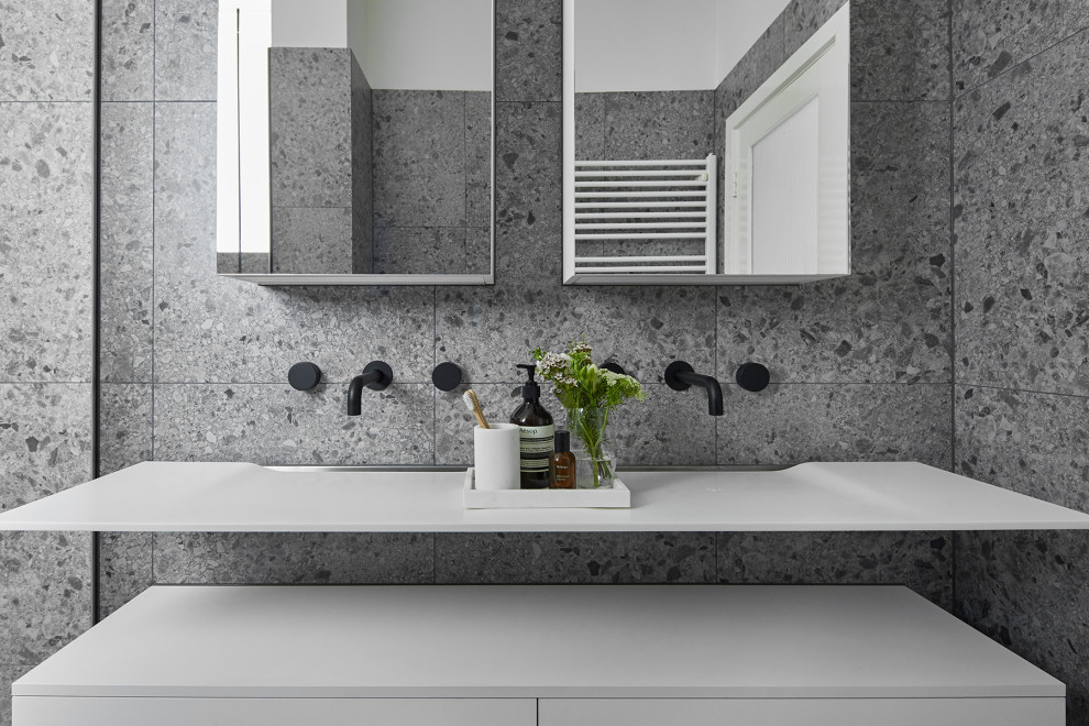 Photo of a medium sized contemporary ensuite bathroom in Melbourne with white cabinets, a double shower, a wall mounted toilet, grey tiles, stone slabs, grey walls, terrazzo flooring, a wall-mounted sink, laminate worktops, grey floors, a hinged door, white worktops and freestanding cabinets.