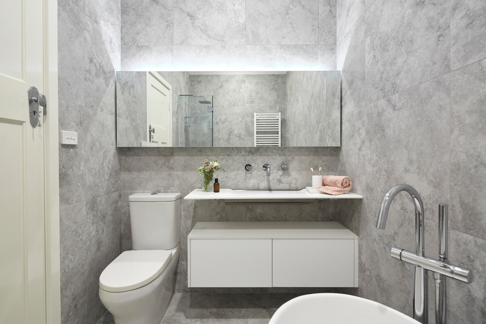 Photo of a small contemporary shower room bathroom in Melbourne with white cabinets, a freestanding bath, a corner shower, a wall mounted toilet, grey tiles, stone tiles, grey walls, marble flooring, a console sink, laminate worktops, grey floors, a hinged door, white worktops and flat-panel cabinets.