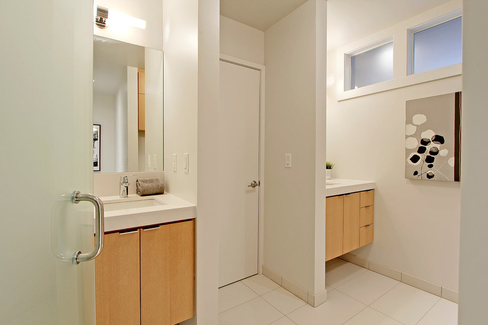 Modelo de cuarto de baño contemporáneo con armarios con paneles lisos, puertas de armario de madera clara, encimera de cuarzo compacto, paredes blancas, suelo de baldosas de porcelana, lavabo bajoencimera y ventanas