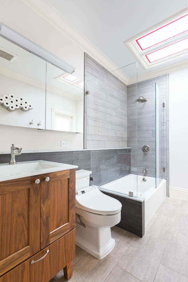 Klassisk inredning av ett mellanstort vit vitt badrum med dusch, med luckor med infälld panel, skåp i mellenmörkt trä, bänkskiva i kvarts, ett hörnbadkar, en dusch/badkar-kombination, en toalettstol med hel cisternkåpa, grå kakel, porslinskakel, vita väggar, klinkergolv i porslin, ett integrerad handfat, beiget golv och med dusch som är öppen