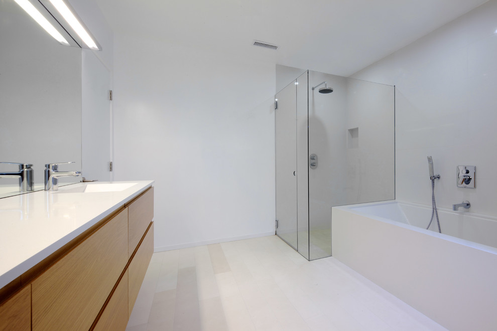 Mid-sized minimalist master white tile and stone tile limestone floor corner shower photo in Los Angeles with an integrated sink, flat-panel cabinets, light wood cabinets, quartz countertops, an undermount tub and white walls