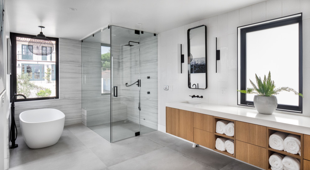 Idéer för att renovera ett funkis en-suite badrum, med släta luckor, skåp i mellenmörkt trä, ett fristående badkar, en kantlös dusch, grå kakel, vit kakel, vita väggar, ett undermonterad handfat, grått golv och dusch med gångjärnsdörr
