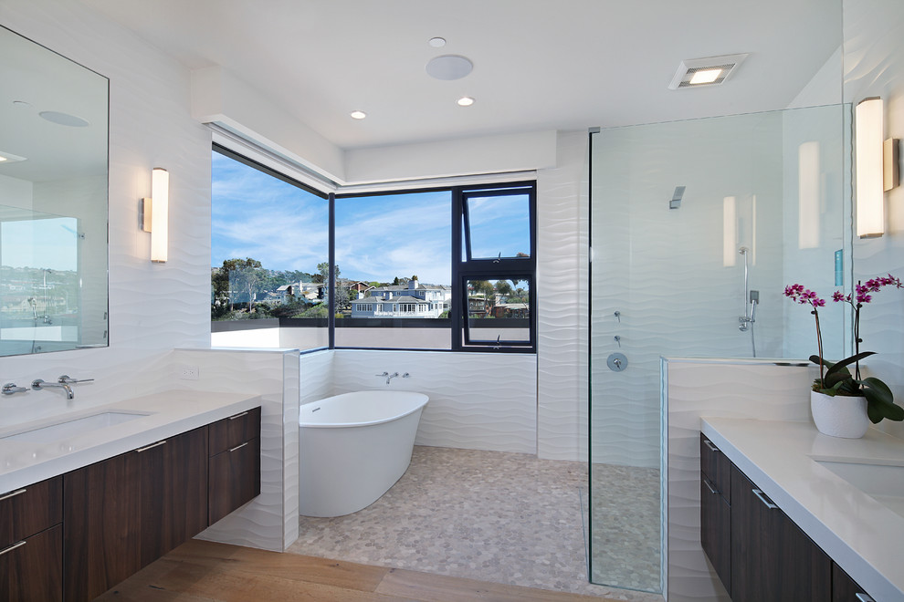Modernes Badezimmer mit flächenbündigen Schrankfronten, dunklen Holzschränken, freistehender Badewanne, bodengleicher Dusche, weißer Wandfarbe, braunem Holzboden und Unterbauwaschbecken in Orange County