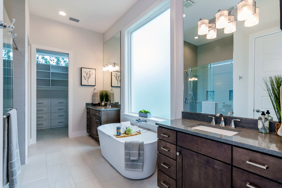 Large modern ensuite bathroom in Orlando with shaker cabinets, dark wood cabinets, a freestanding bath, a double shower, a one-piece toilet, grey tiles, ceramic tiles, grey walls, porcelain flooring, a submerged sink, engineered stone worktops, grey floors, a sliding door and grey worktops.
