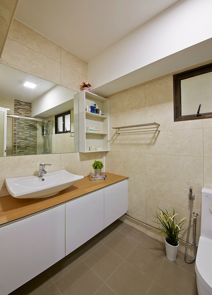 Mittelgroßes Modernes Badezimmer En Suite mit profilierten Schrankfronten, hellbraunen Holzschränken, Waschtisch aus Holz, Toilette mit Aufsatzspülkasten, grauen Fliesen, beiger Wandfarbe und Schieferboden in Singapur