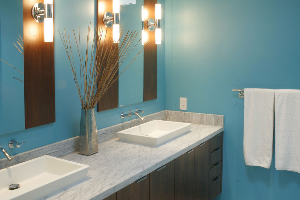 Modelo de cuarto de baño principal moderno de tamaño medio con armarios con paneles lisos, puertas de armario de madera en tonos medios, paredes azules, lavabo sobreencimera y encimera de mármol