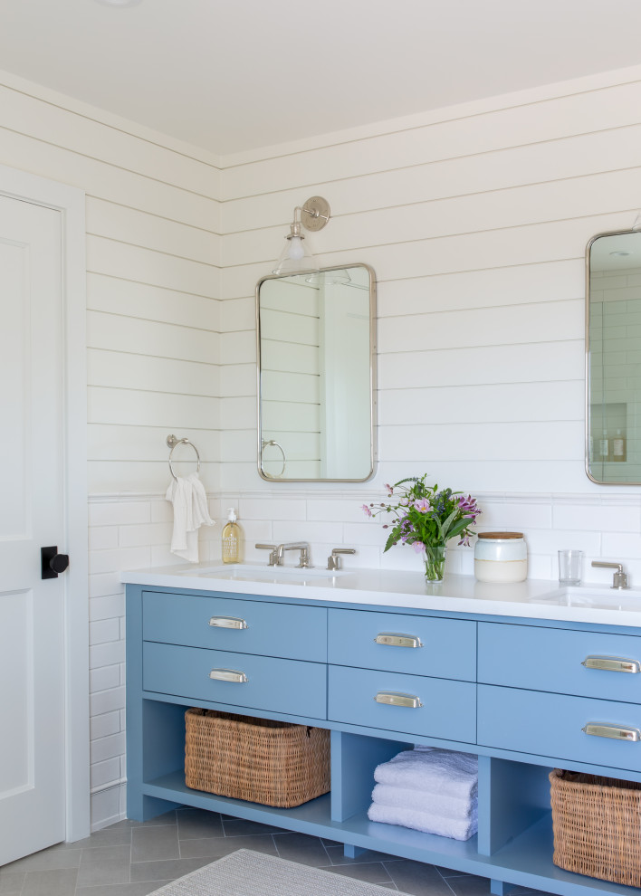 Lantlig inredning av ett vit vitt badrum, med släta luckor, blå skåp, vit kakel, tunnelbanekakel, vita väggar och ett undermonterad handfat