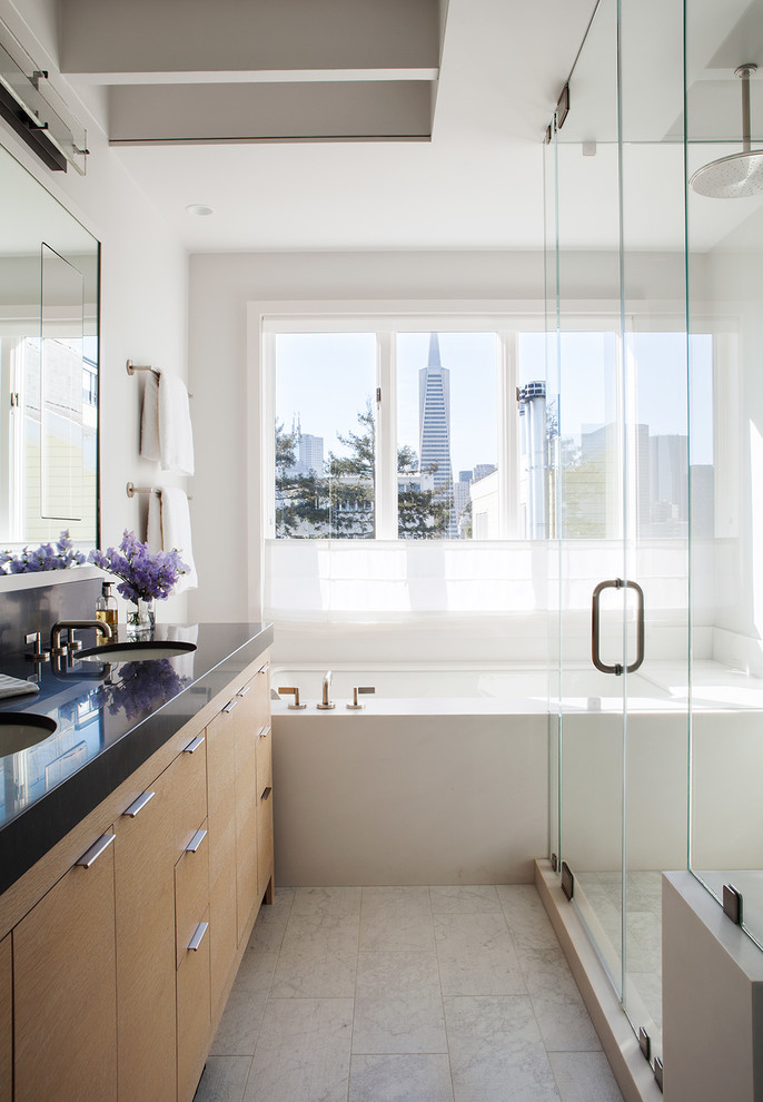 Aménagement d'une salle de bain contemporaine en bois clair avec un lavabo encastré, un placard à porte plane, une baignoire encastrée, un mur blanc et une fenêtre.