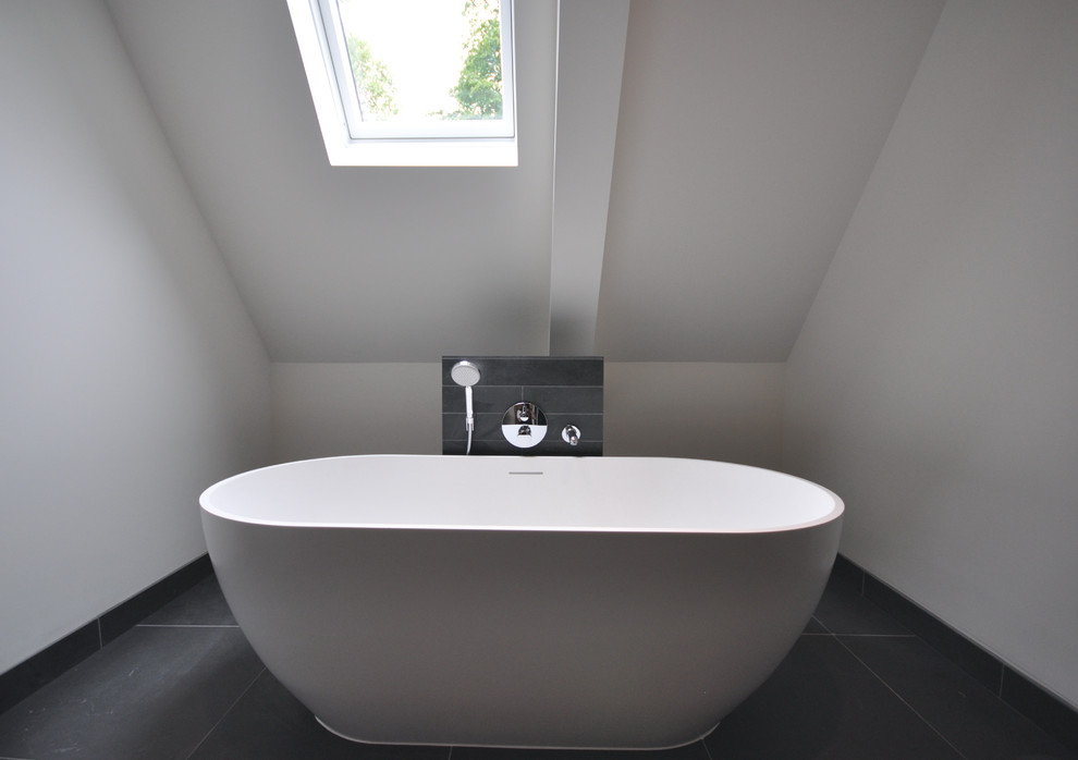 Inspiration for a large contemporary family bathroom in Wiltshire with white cabinets, a freestanding bath, a walk-in shower, a wall mounted toilet, black tiles, stone slabs, white walls, travertine flooring, a wall-mounted sink and tiled worktops.