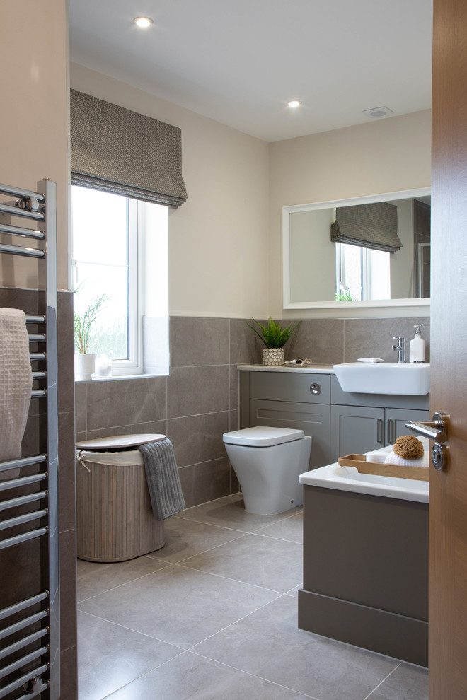 Imagen de cuarto de baño clásico renovado con armarios estilo shaker, puertas de armario grises, sanitario de una pieza, baldosas y/o azulejos grises, paredes beige, suelo gris y encimeras blancas