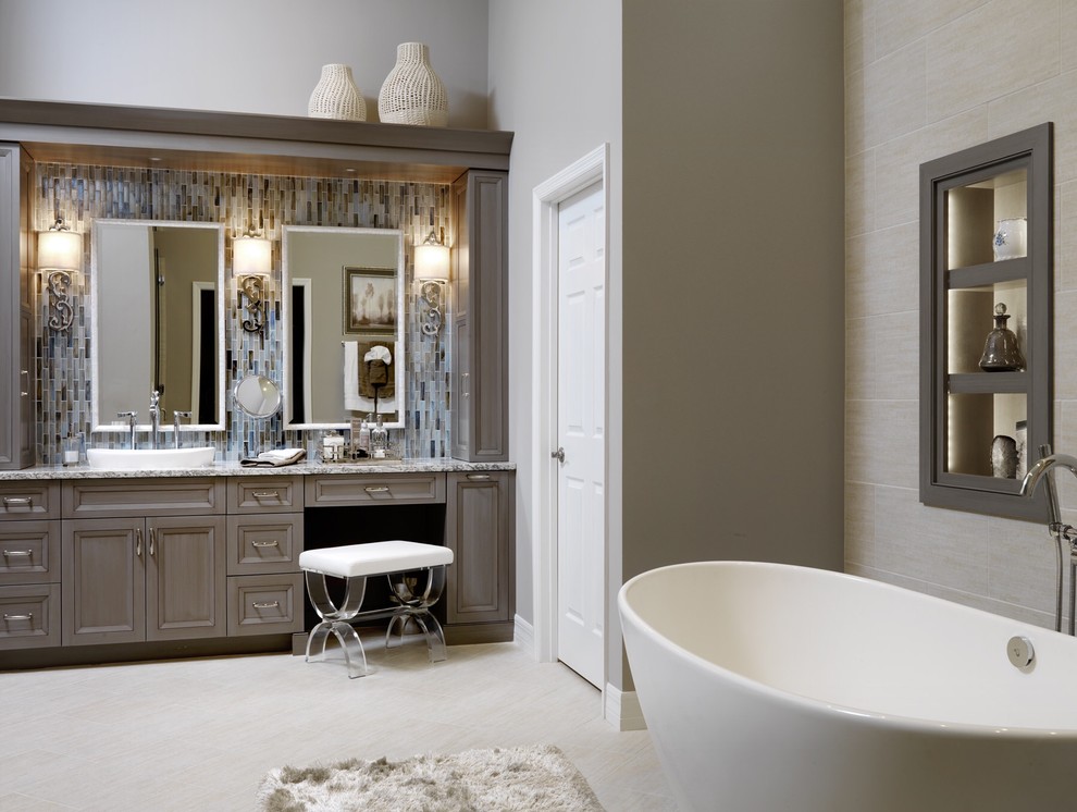 Exempel på ett mellanstort klassiskt en-suite badrum, med luckor med infälld panel, grå skåp, ett fristående badkar, en toalettstol med hel cisternkåpa, beige kakel, grå kakel, glaskakel, beige väggar, vinylgolv, ett fristående handfat och granitbänkskiva