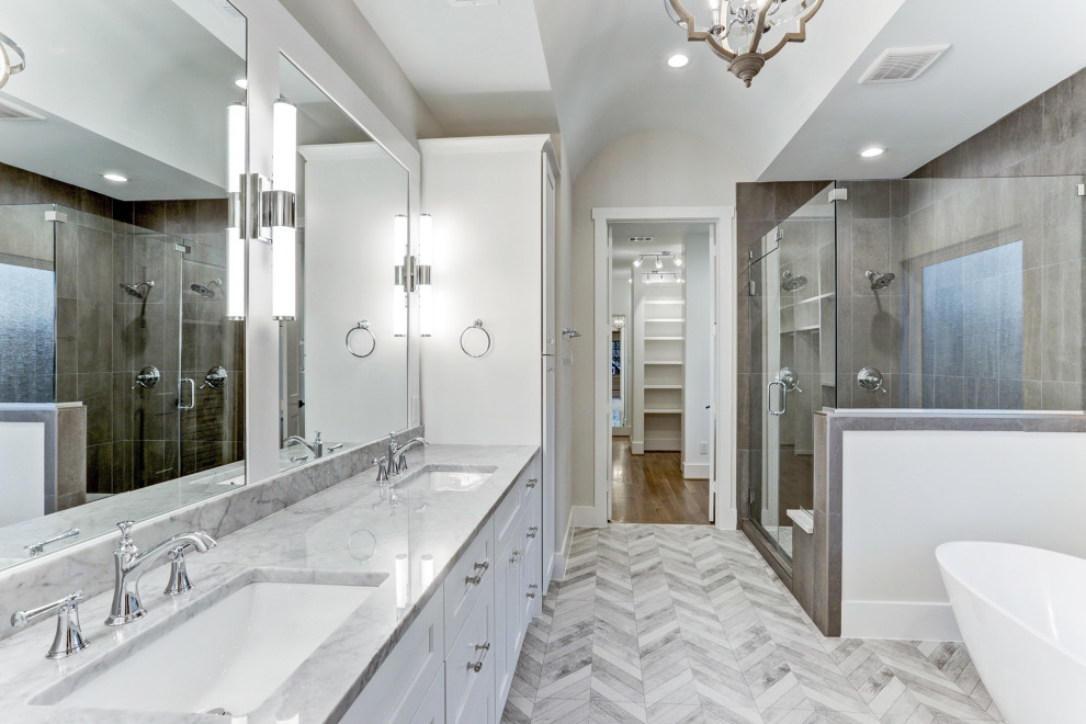 This is an example of a large traditional bathroom in Houston with shaker cabinets, white cabinets, a freestanding bath, a corner shower, porcelain tiles, white walls, porcelain flooring, a submerged sink, marble worktops, grey floors and grey worktops.