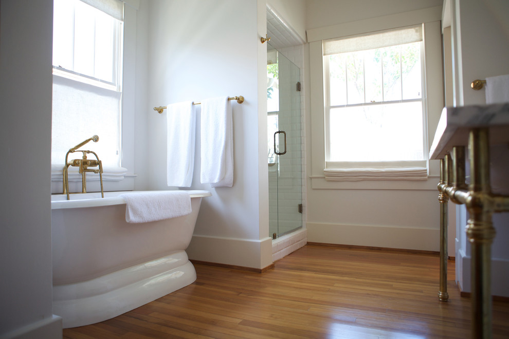 Idéer för att renovera ett mellanstort amerikanskt en-suite badrum, med släta luckor, vita skåp, ett badkar med tassar, en dusch i en alkov, en toalettstol med hel cisternkåpa, vit kakel, tunnelbanekakel, vita väggar, mellanmörkt trägolv, ett konsol handfat och marmorbänkskiva