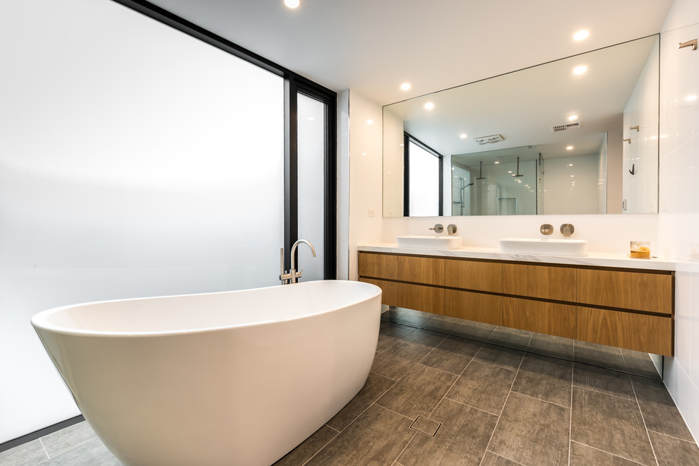 На фото: главная ванная комната среднего размера в современном стиле с плоскими фасадами, светлыми деревянными фасадами, отдельно стоящей ванной, двойным душем, унитазом-моноблоком, белой плиткой, цементной плиткой, белыми стенами, полом из керамической плитки, настольной раковиной, мраморной столешницей, серым полом, открытым душем и белой столешницей