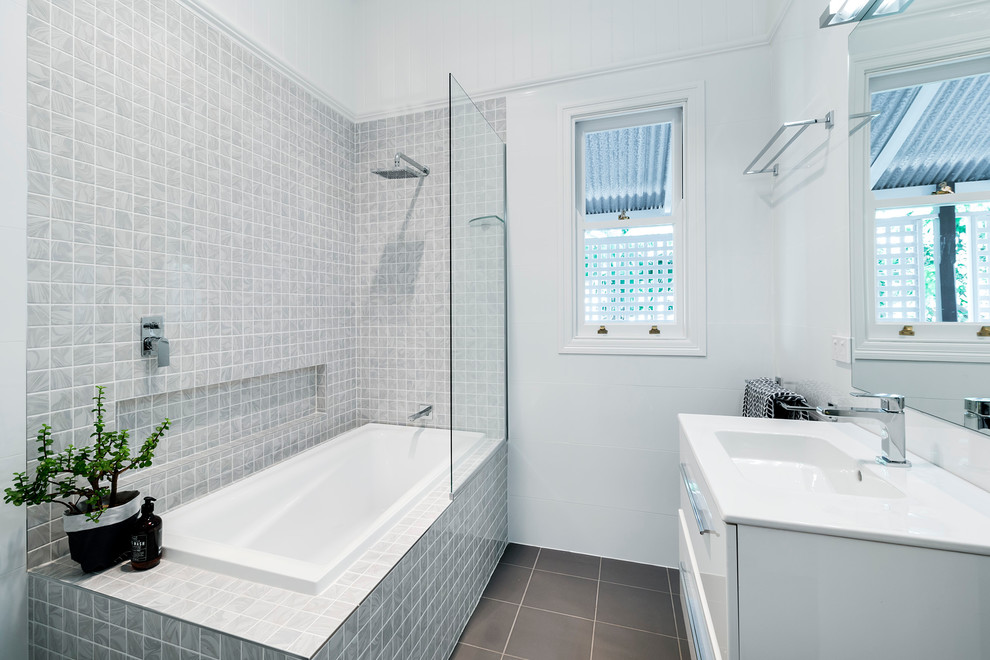 Cette image montre une petite salle d'eau minimaliste avec un placard à porte plane, des portes de placard blanches, une baignoire posée, un combiné douche/baignoire, un carrelage gris, des carreaux de céramique, un mur blanc et un sol en carrelage de céramique.