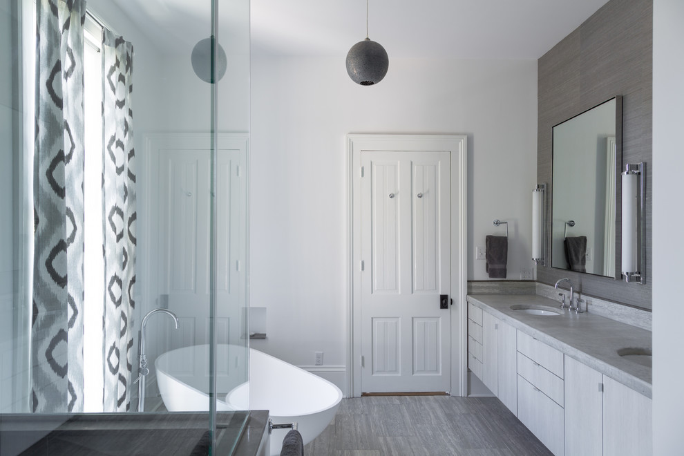 This is an example of a medium sized contemporary ensuite bathroom in New Orleans with flat-panel cabinets, a freestanding bath, a corner shower, a two-piece toilet, white walls, lino flooring, a submerged sink, limestone worktops and grey cabinets.