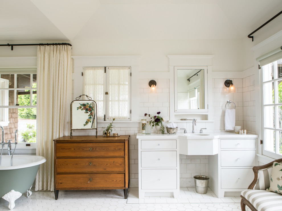 Cette image montre une salle de bain principale craftsman avec un placard à porte plane, des portes de placard blanches, une baignoire sur pieds, un carrelage blanc, un mur blanc, un lavabo encastré, un sol blanc et un plan de toilette blanc.