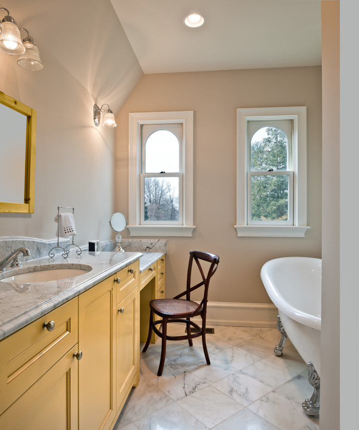 Идея дизайна: главная ванная комната среднего размера в классическом стиле с плоскими фасадами, желтыми фасадами, ванной на ножках, раздельным унитазом, белой плиткой, бежевыми стенами, врезной раковиной, душем в нише, каменной плиткой, мраморным полом и мраморной столешницей