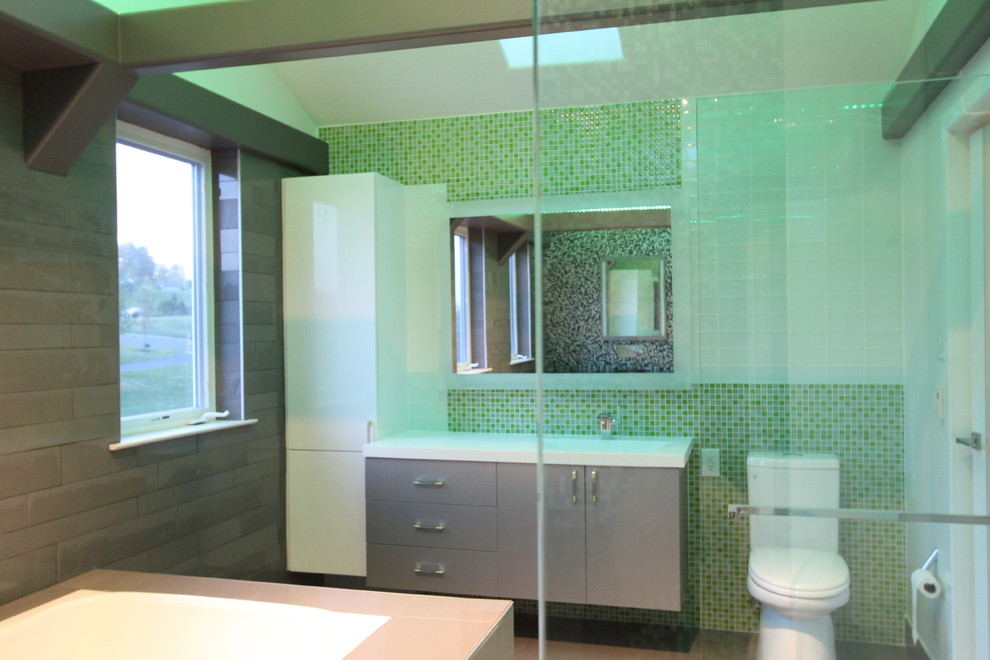 На фото: главная ванная комната среднего размера в современном стиле с стеклянными фасадами, зелеными фасадами, полновстраиваемой ванной, открытым душем, унитазом-моноблоком, зеленой плиткой, стеклянной плиткой, зелеными стенами, полом из керамогранита, монолитной раковиной и столешницей из искусственного камня с