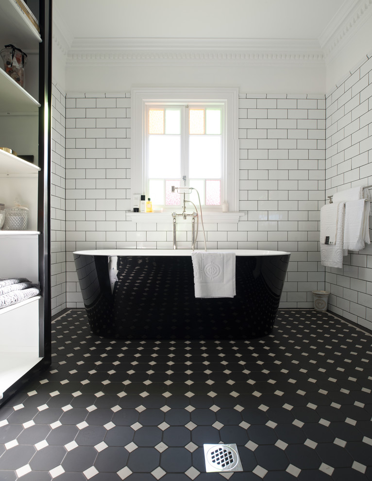 Cette image montre une grande salle de bain principale design avec une baignoire indépendante, un carrelage blanc, un carrelage métro, un mur blanc, un sol en carrelage de porcelaine, un lavabo de ferme et un sol noir.