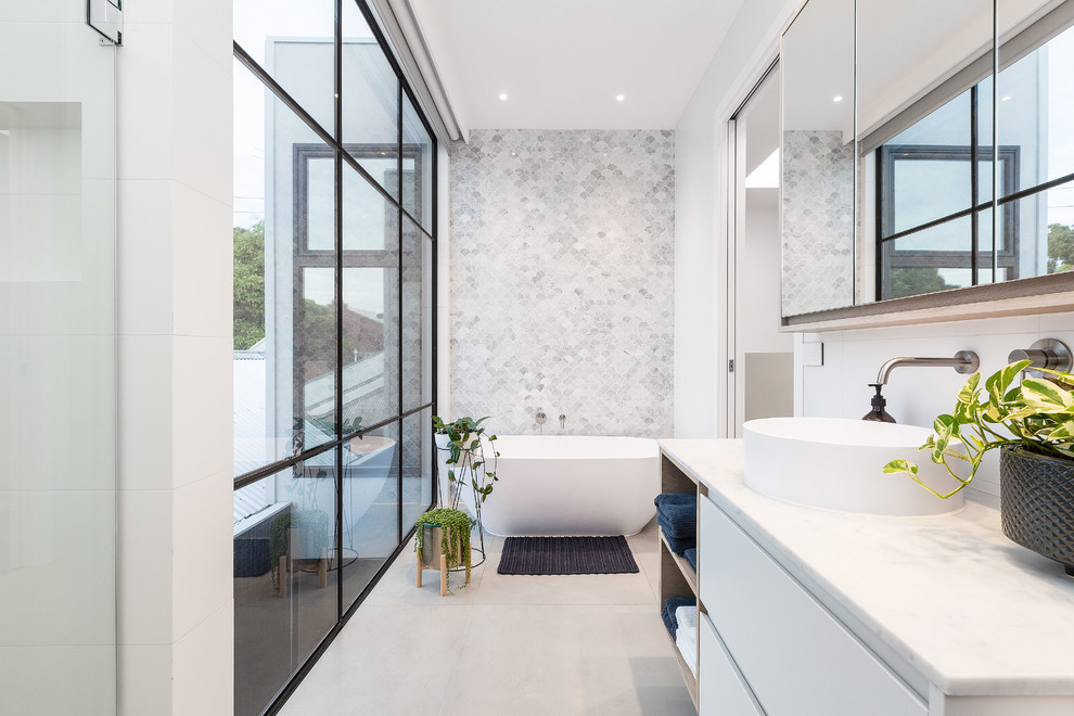 Источник вдохновения для домашнего уюта: главная ванная комната среднего размера в современном стиле с плоскими фасадами, белыми фасадами, отдельно стоящей ванной, серой плиткой, мраморной плиткой, белыми стенами, бетонным полом, настольной раковиной, серым полом, душевой комнатой, мраморной столешницей, душем с распашными дверями и белой столешницей