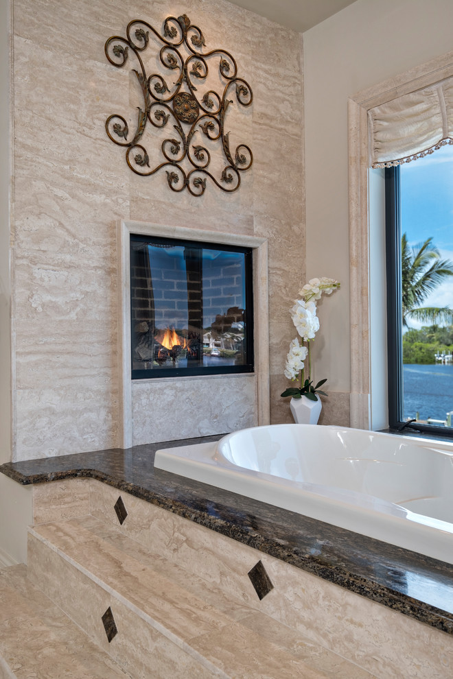 This is an example of a large mediterranean ensuite bathroom in Miami with a built-in bath, beige tiles, stone slabs, beige walls, travertine flooring, a built-in sink, marble worktops and beige floors.