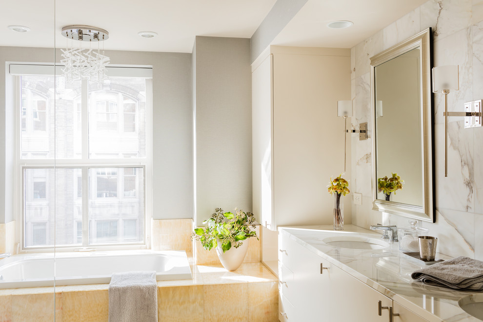 Medium sized contemporary ensuite bathroom in Boston with flat-panel cabinets, white cabinets, a built-in bath, a corner shower, a one-piece toilet, white tiles, stone slabs, grey walls, marble flooring, a submerged sink and marble worktops.