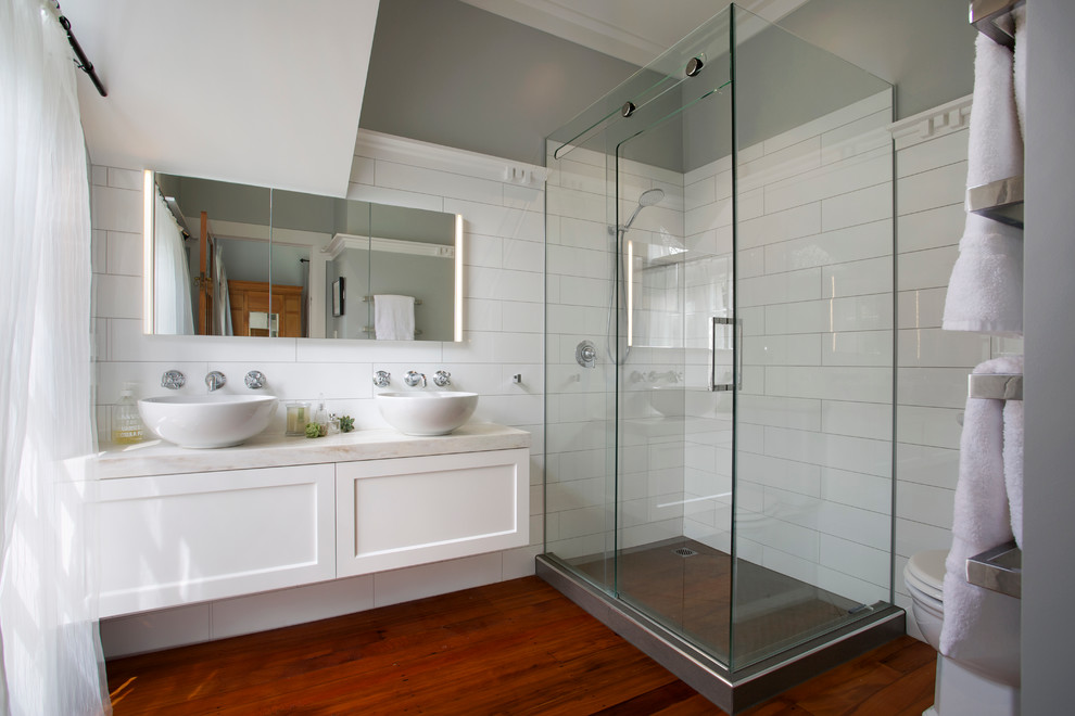 Exemple d'une salle de bain chic avec un placard à porte shaker, des portes de placard blanches, une douche d'angle, un carrelage blanc, des carreaux de céramique, un mur gris, une vasque et un plan de toilette en surface solide.