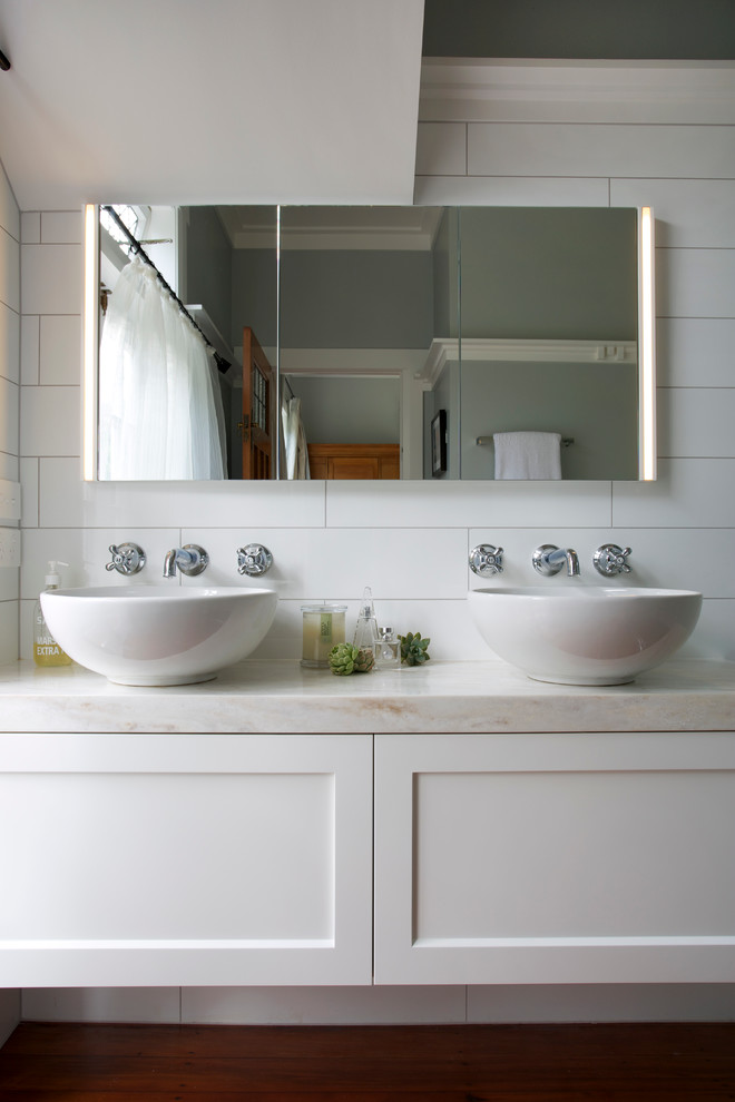 Пример оригинального дизайна: ванная комната в классическом стиле с фасадами с утопленной филенкой, белыми фасадами, белой плиткой, серыми стенами, настольной раковиной и столешницей из искусственного камня