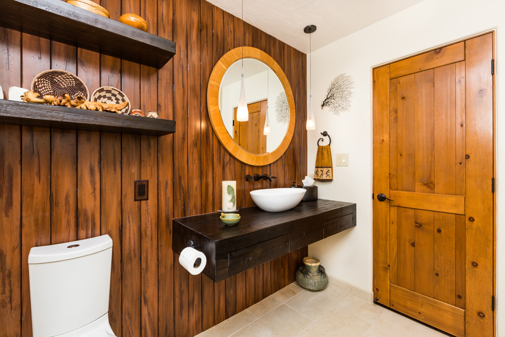 アルバカーキにある高級な中くらいなサンタフェスタイルのおしゃれなバスルーム (浴槽なし) (ベッセル式洗面器、濃色木目調キャビネット、木製洗面台、ベージュの壁、分離型トイレ、磁器タイルの床) の写真