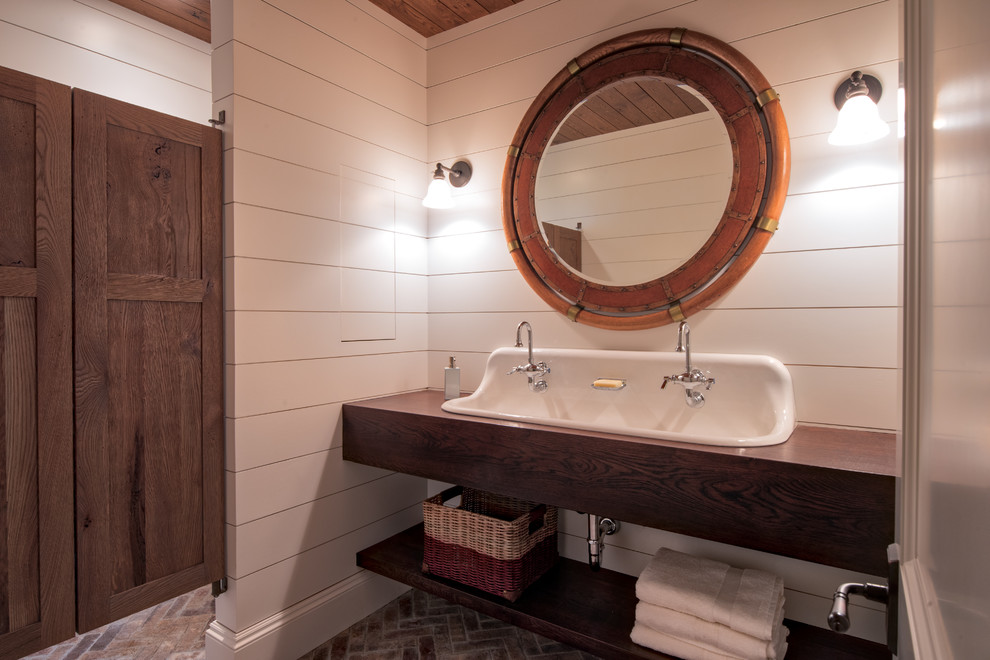 Klassisk inredning av ett mellanstort badrum med dusch, med öppna hyllor, skåp i mörkt trä, vita väggar, tegelgolv, ett avlångt handfat, träbänkskiva och rött golv
