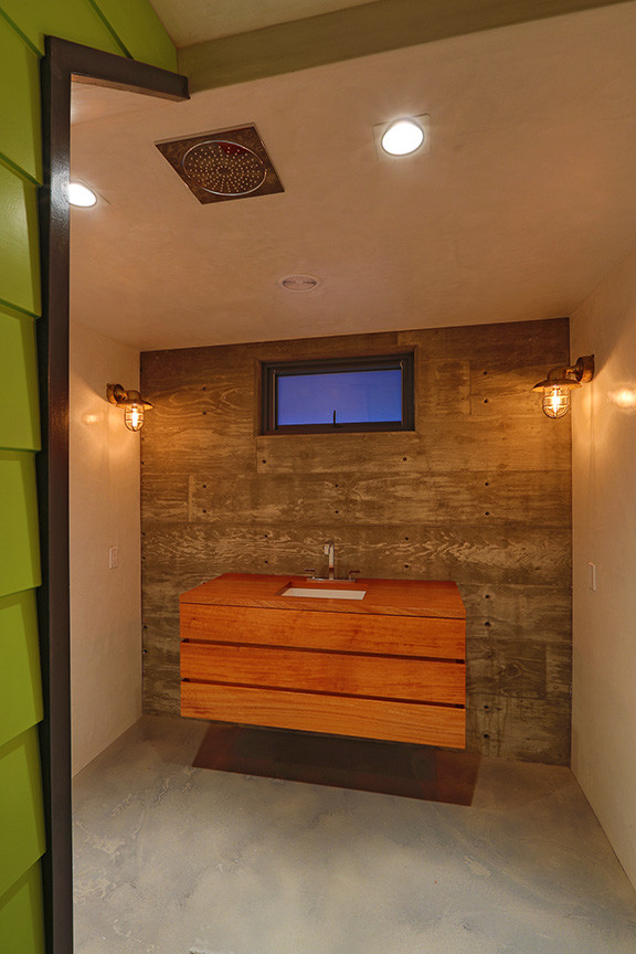 Exotisk inredning av ett stort badrum med dusch, med släta luckor, skåp i mellenmörkt trä, en toalettstol med separat cisternkåpa, grå väggar, betonggolv, ett undermonterad handfat och träbänkskiva