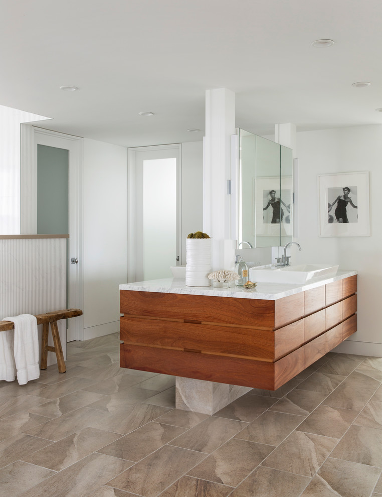 This is an example of a large contemporary ensuite bathroom in Los Angeles with flat-panel cabinets, medium wood cabinets, a walk-in shower, white tiles, ceramic tiles, white walls, marble worktops, a two-piece toilet, marble flooring and a console sink.