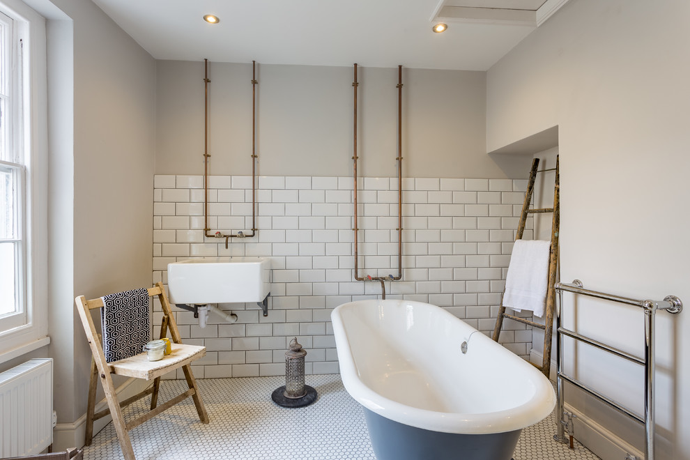 Diseño de cuarto de baño industrial de tamaño medio con bañera exenta, paredes grises, lavabo suspendido y suelo blanco