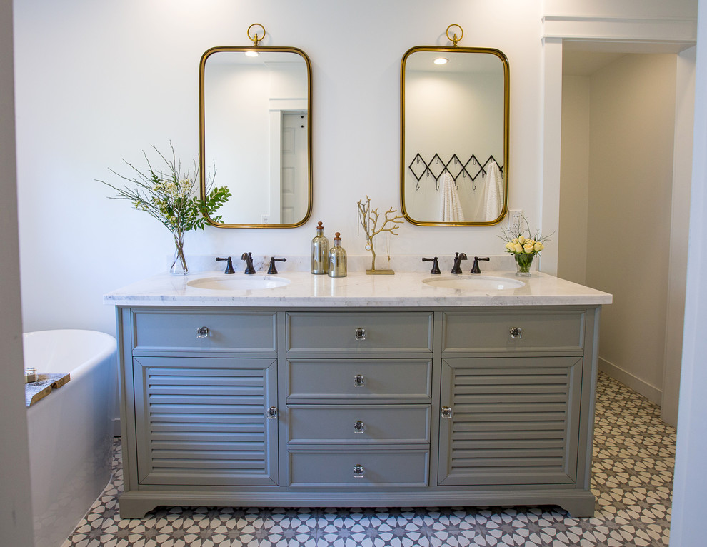 Inspiration for a medium sized country ensuite bathroom in Los Angeles with louvered cabinets, grey cabinets, a freestanding bath, an alcove shower, a one-piece toilet, white tiles, ceramic tiles, white walls, cement flooring, a submerged sink, marble worktops, grey floors and a hinged door.