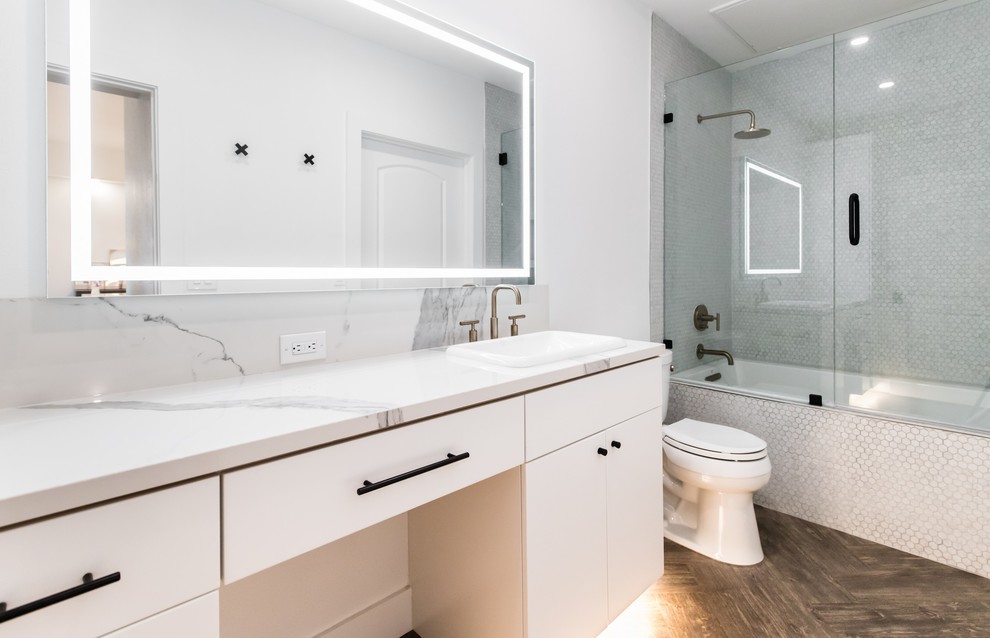 На фото: маленькая главная ванная комната в стиле модернизм с плоскими фасадами, белыми фасадами, накладной ванной, душем над ванной, унитазом-моноблоком, серой плиткой, плиткой мозаикой, белыми стенами, полом из винила, накладной раковиной, стеклянной столешницей, коричневым полом, душем с распашными дверями и белой столешницей для на участке и в саду