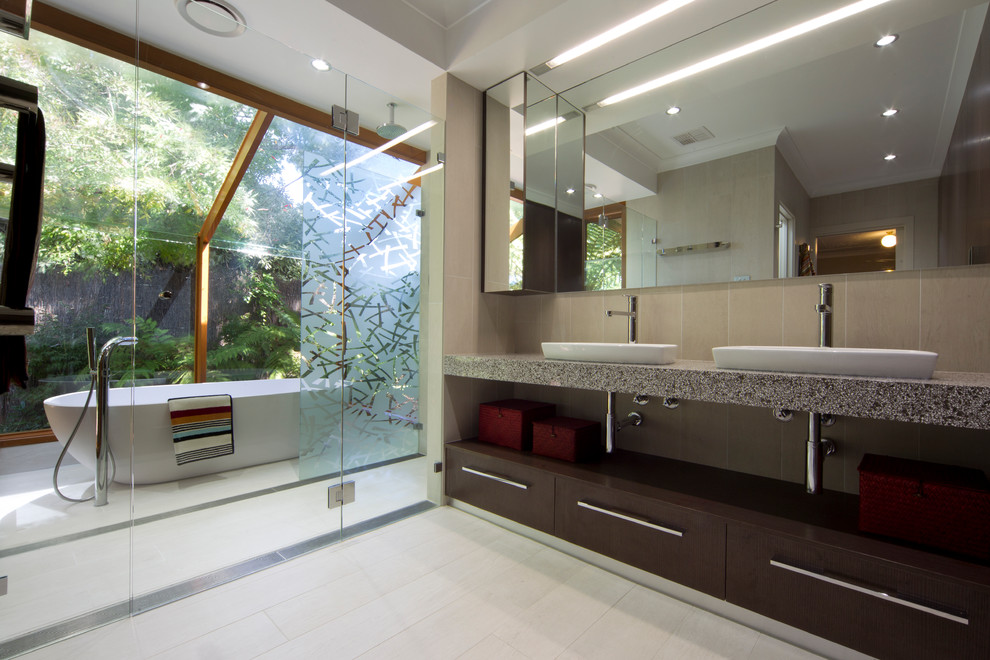 Пример оригинального дизайна: ванная комната в современном стиле с накладной раковиной, плоскими фасадами, темными деревянными фасадами, отдельно стоящей ванной и бежевой плиткой
