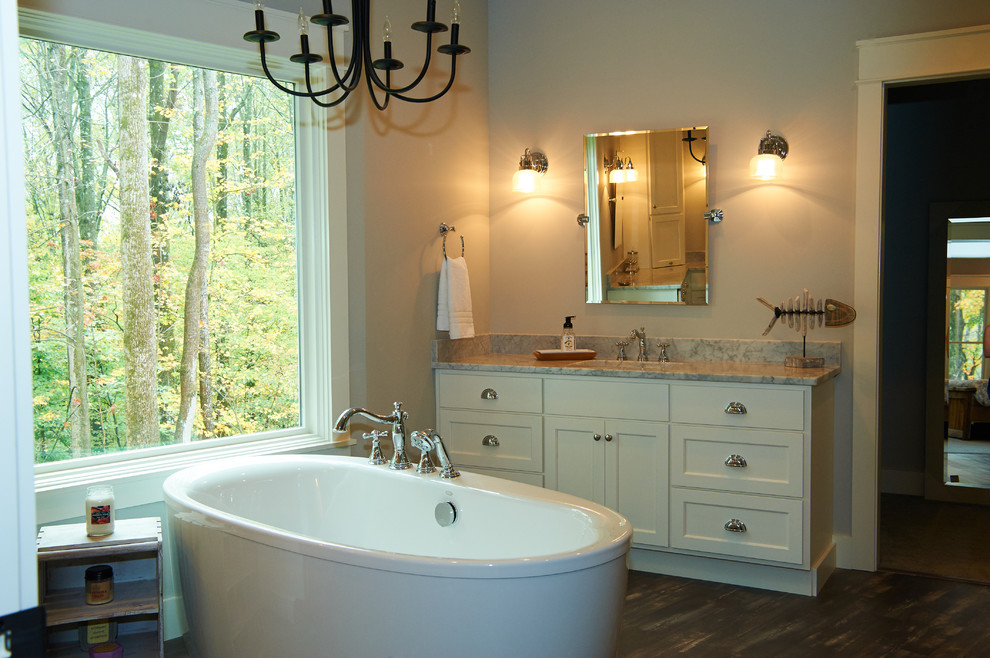 Inspiration for a large rural ensuite bathroom in Indianapolis with shaker cabinets, white cabinets, a freestanding bath, an alcove shower, a two-piece toilet, white tiles, ceramic tiles, grey walls, vinyl flooring, a submerged sink, marble worktops, grey floors and a hinged door.