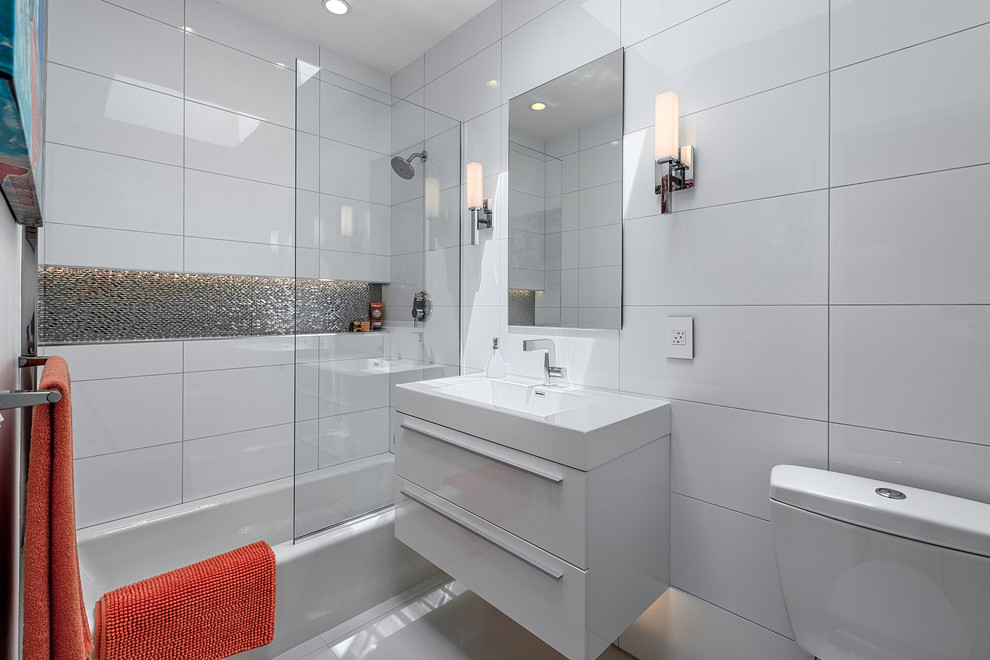 Inredning av ett 50 tals badrum, med ett integrerad handfat, släta luckor, vita skåp, ett badkar i en alkov, en dusch/badkar-kombination och vit kakel
