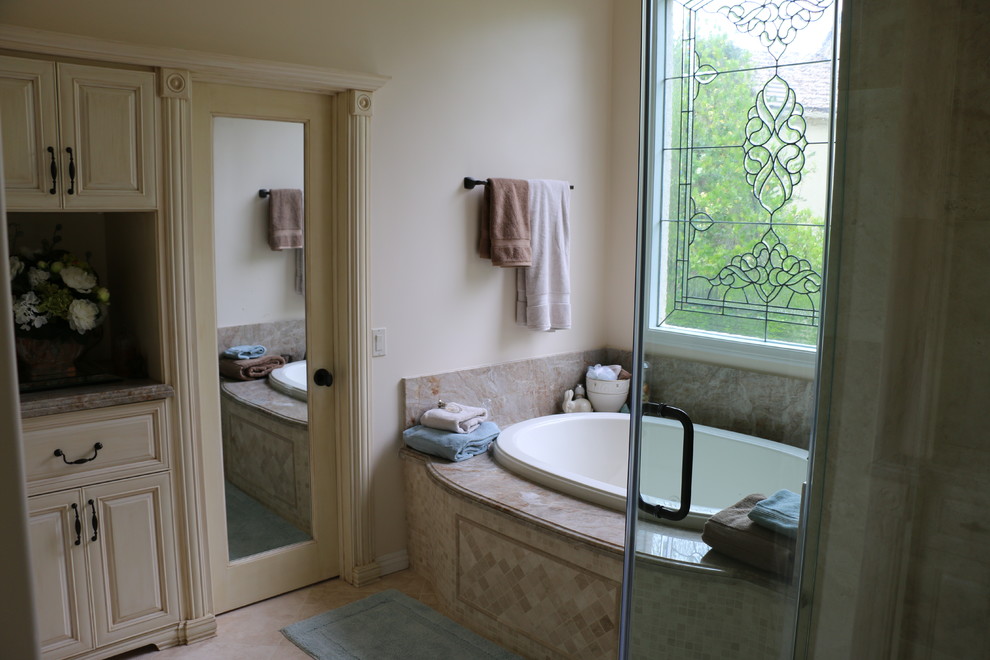 This is an example of a large classic ensuite bathroom in Los Angeles with a submerged sink, beige cabinets, granite worktops, a built-in bath, a walk-in shower, a one-piece toilet, beige tiles, stone tiles and beige walls.
