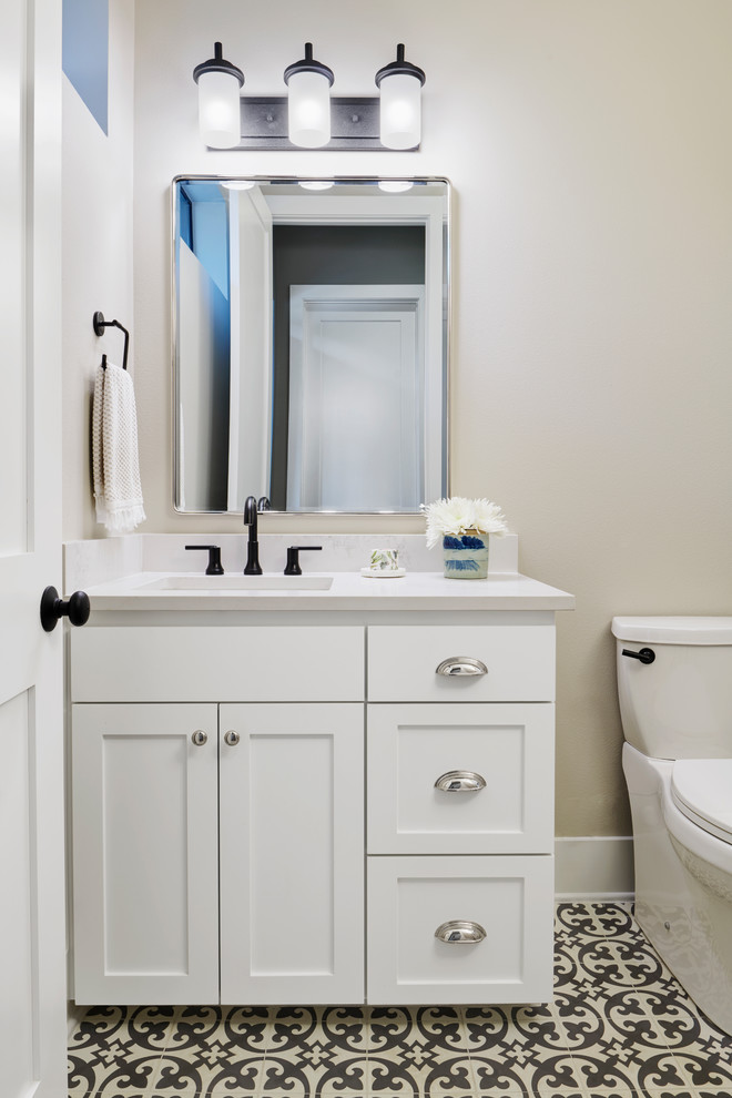 Cette image montre une salle de bain traditionnelle avec un placard à porte shaker, des portes de placard blanches, un sol multicolore, WC séparés, un mur beige, un plan de toilette blanc et un lavabo encastré.