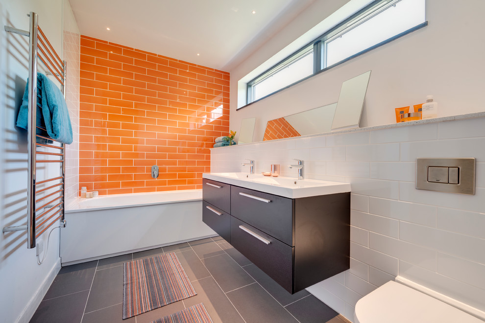 Diseño de cuarto de baño actual con armarios con paneles lisos, puertas de armario de madera en tonos medios, bañera empotrada, baldosas y/o azulejos naranja, paredes blancas y suelo gris