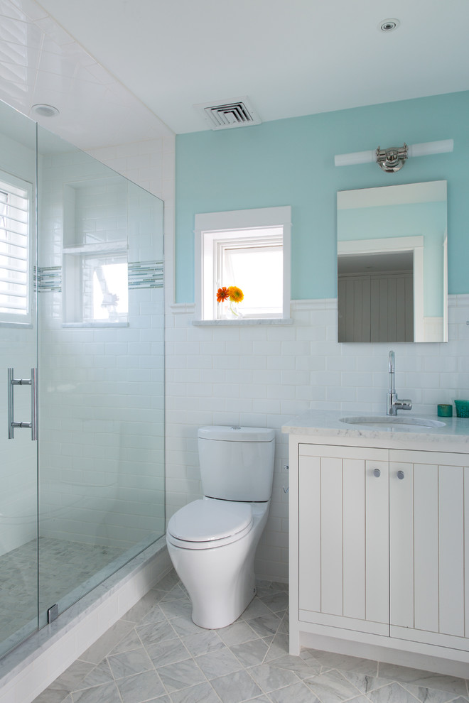 Photo of a small beach style ensuite bathroom in Portland Maine with a submerged sink, flat-panel cabinets, white cabinets, marble worktops, an alcove shower, a two-piece toilet, white tiles, ceramic tiles, blue walls and marble flooring.