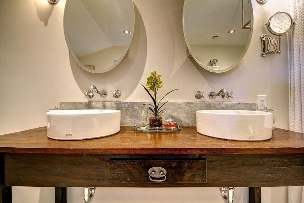 Foto di una stanza da bagno country con lavabo a bacinella, consolle stile comò, ante in legno bruno, top in legno e pareti bianche