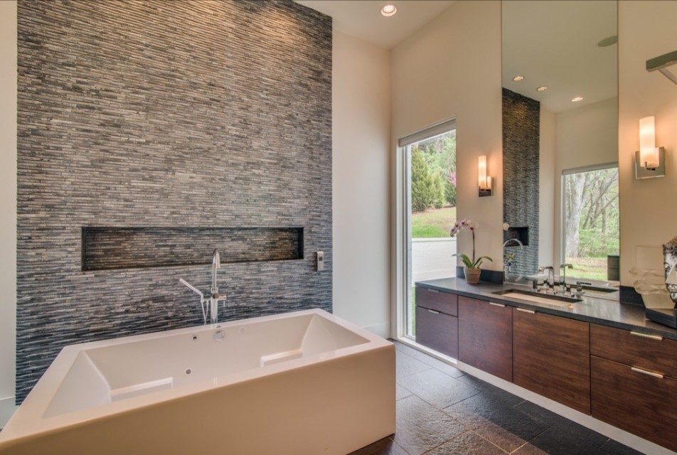 Exemple d'une salle de bain principale moderne en bois foncé de taille moyenne avec un placard à porte plane, une baignoire indépendante, un carrelage noir, un carrelage de pierre, un mur beige, un sol en travertin, un lavabo encastré et un plan de toilette en surface solide.