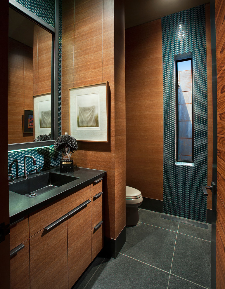 Cette image montre une grande salle d'eau sud-ouest américain en bois brun avec un placard à porte plane, un carrelage bleu, mosaïque, un sol en ardoise, un lavabo posé, un plan de toilette en onyx et un sol noir.